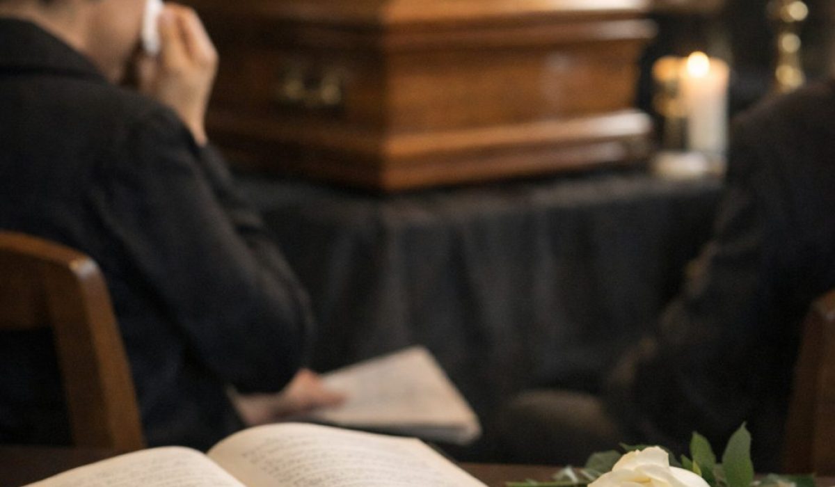 Table avec livre ouvert, lettres manuscrites et rose blanche devant une scène d’enterrement en intérieur